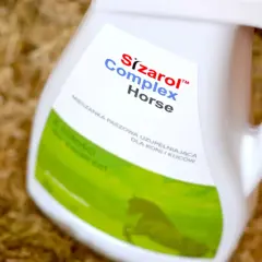 Biały kanister z etykietą "Sizarol Complex Horse" na tle ściółki dla zwierząt.