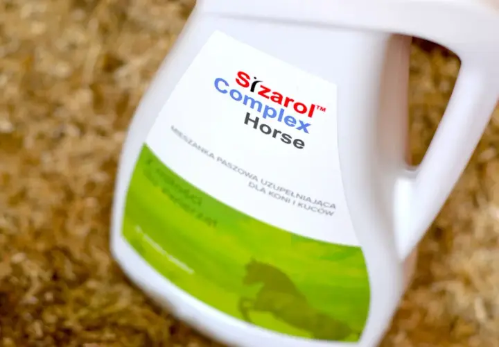 Biały kanister z etykietą "Sizarol Complex Horse" na tle ściółki dla zwierząt.