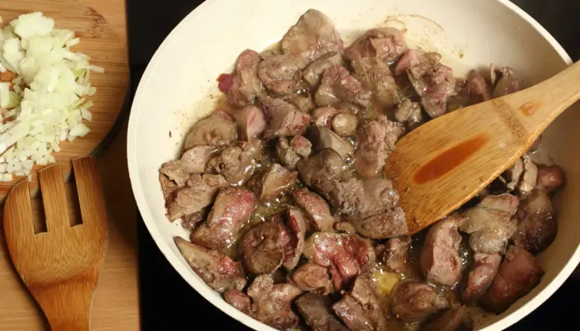 Smażona wątróbka na patelni, obok posiekana cebula. Czy pies może jeść wątróbkę? Tak, ale z umiarem.
